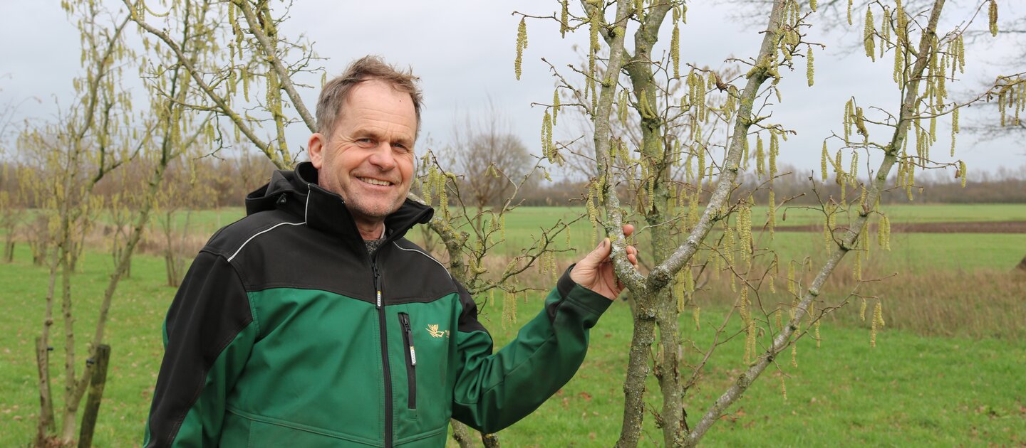 man lacht naast kale boom in weiland